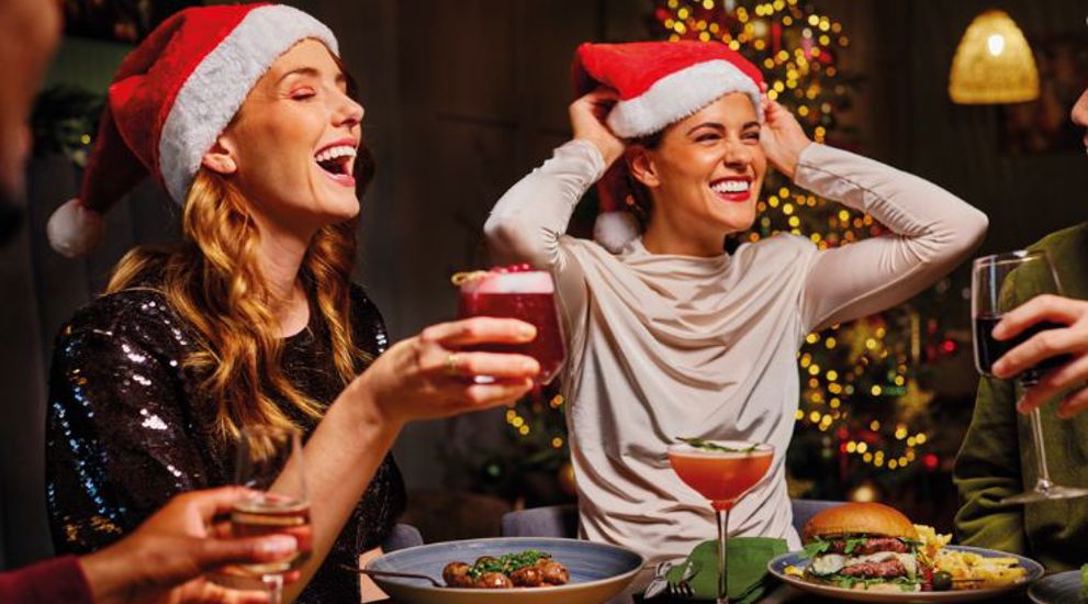Two girls wearing Santa hats while they eat a Christmas meal 